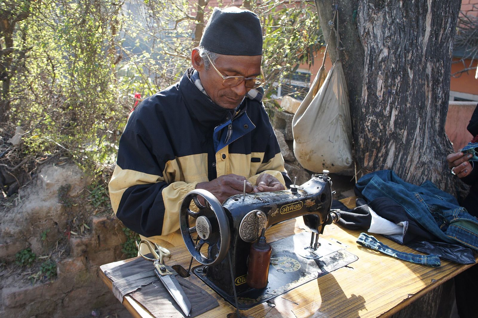 An old tailor working at his sewing machine under a tree at Swayambhunath