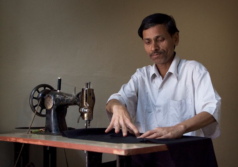 A tailor smoothing dark cloth at his sewing machine