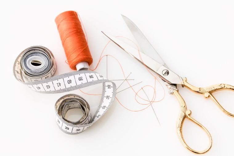 A tape measure, thread and gold scissors on white