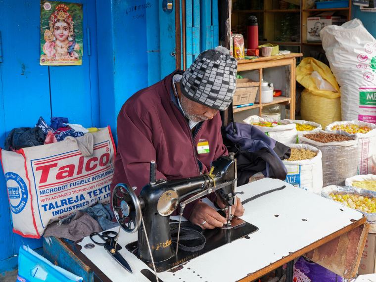A tailor in a dhaka topi working at his sewing machine